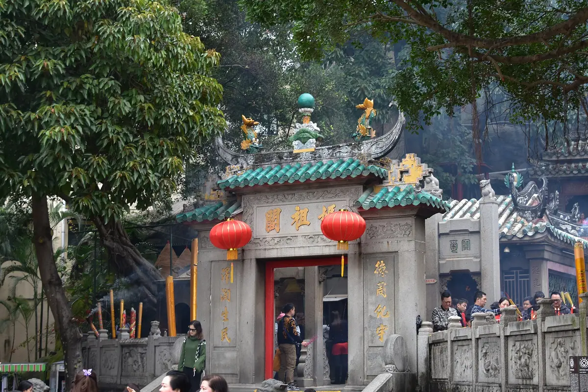 The green-tiled gate pavilion of A-Ma Temple with red lanterns and visitors burning incense
