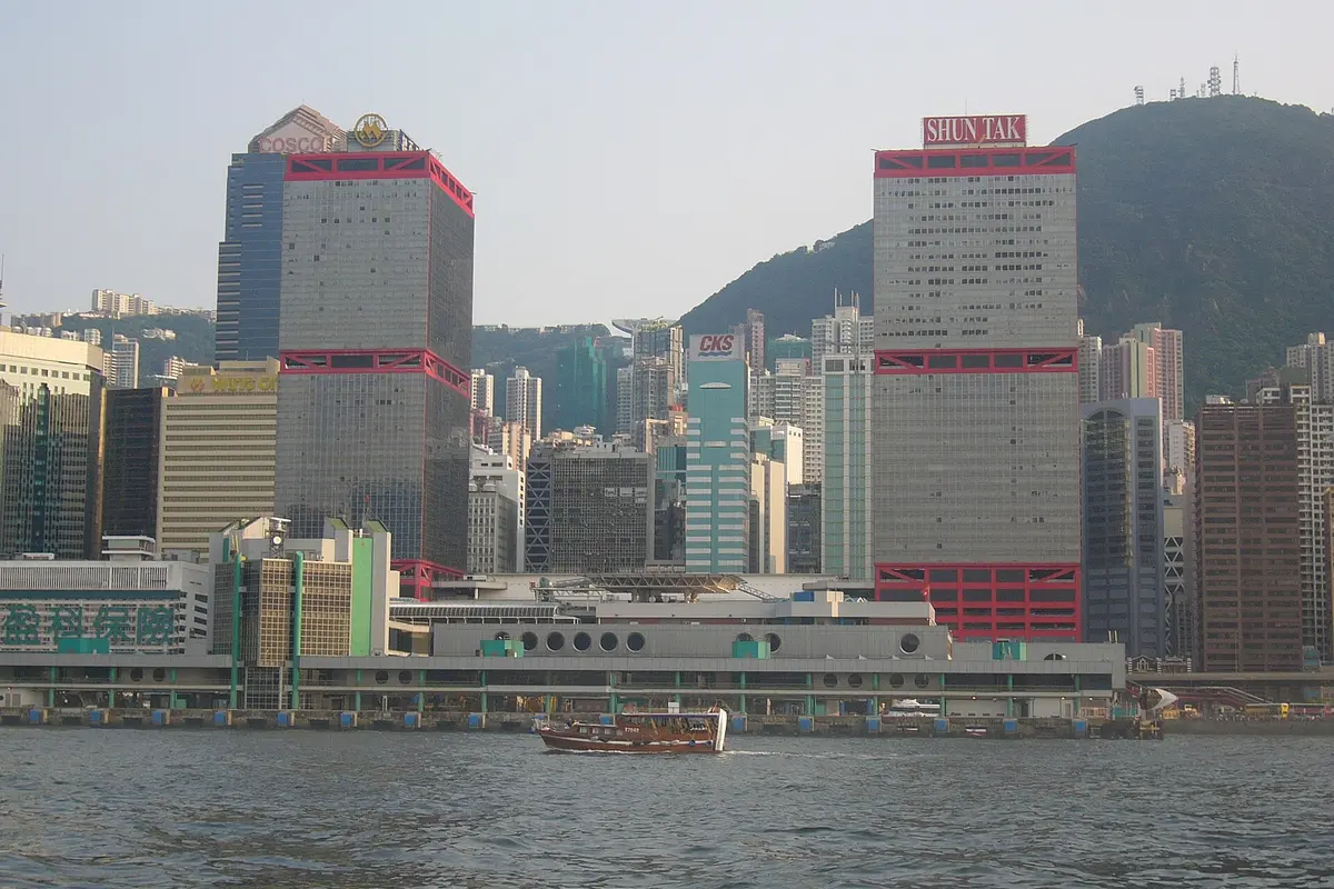 The Shun Tak Centre towers and the low ferry terminal building on the Hong Kong Island waterfront, seen across the harbour with a small boat in the foreground